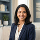 A smiling South Asian woman with radiant skin, captured in a professional headshot against a soft-toned, modern background.